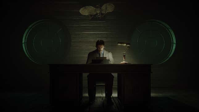 Alan Wake sits at a desk in front of a typewriter, in a dark room with two round windows behind him.
